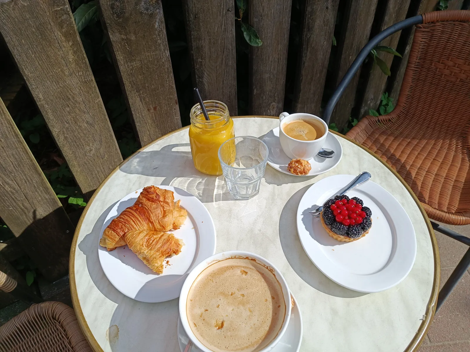 Frühstückstisch für zwei mit Croissants, Milchkaffee, Espresso, Orangensaft und Tartelette