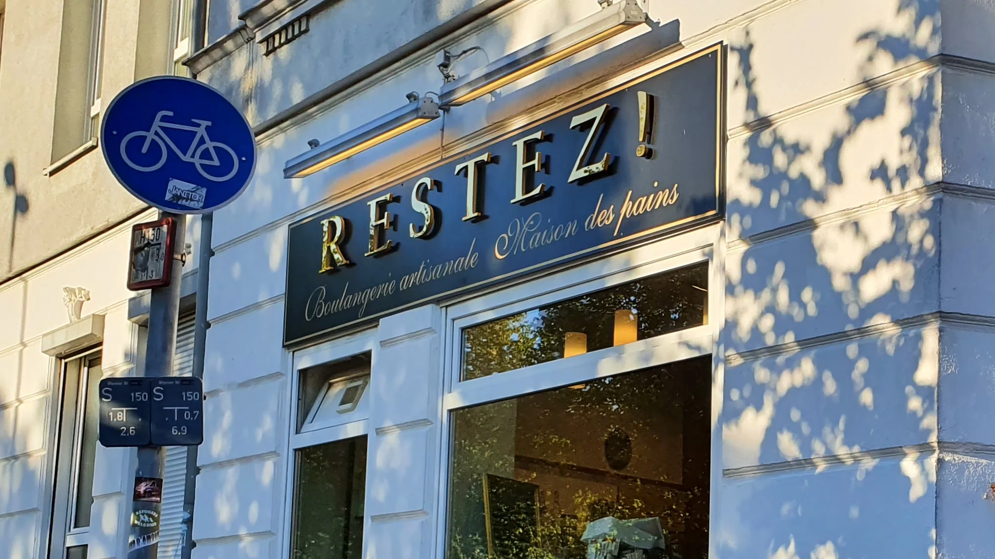Fassade der Sternstraße mit dem Schriftzug „Restez!“ im Schattenlicht der Bäume