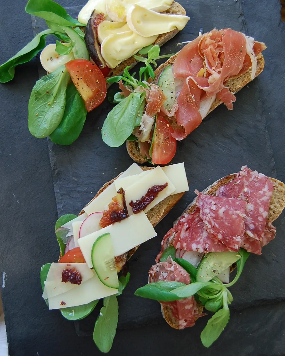 Belegte Tartines mit Schinken, Käse, Salami und Salat auf einer Schieferplatte